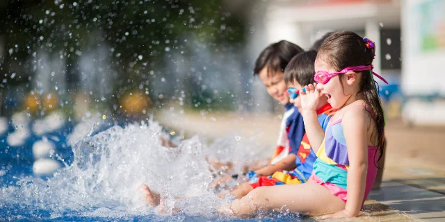 Children in goggles sitting on the pool edge, kicking up splashes