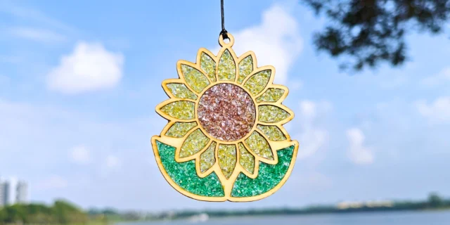 A glittery sunflower suncatcher hanging against a blue sky by the bay