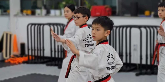 Children in white taekwondo uniforms practising a stance in class