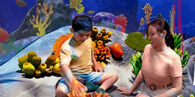 A boy and a woman playing among coral and sea creature models at Curiosity Cove