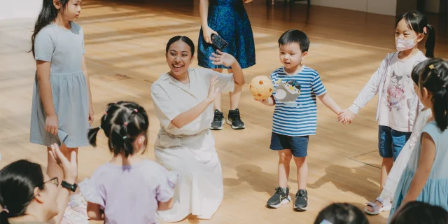 A facilitator and young children holding hands in a circle during a story session