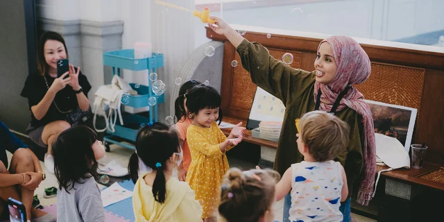 A facilitator blowing bubbles for a group of toddlers at National Gallery Singapore