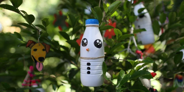 A snowman ornament made from a plastic bottle hanging on a tree among other handmade decorations