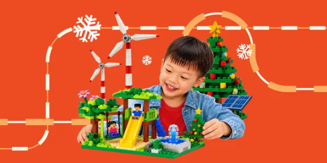 A smiling boy beside a LEGO playground build with wind turbines and a Christmas tree